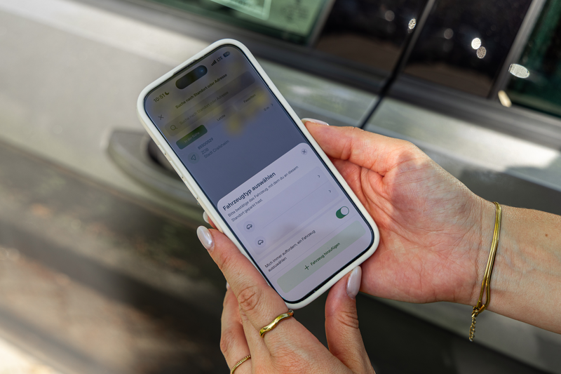 eine Frau hat eine Handy in der Hand mit der geöffneten paybyphone-App am Auto